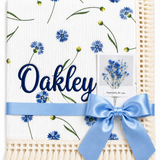 Cornflower Meadow muslin baby blanket with blue flowers, Oakley embroidered in navy, cream fringe and blue ribbon.
