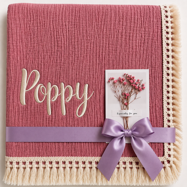 Dusty Pink muslin baby blanket personalised with Poppy in cream embroidery, a fringed border and lilac ribbon.